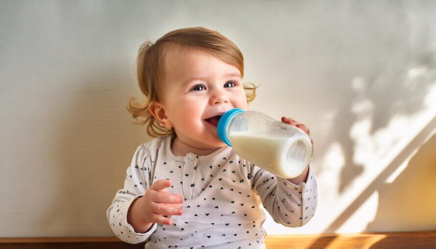 A happy baby drinking a bottle of milk and smiling cheerfully